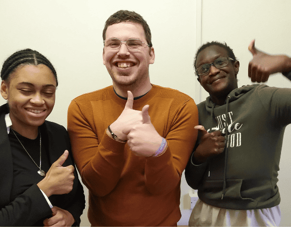Three people standing together with their thumbs up smiling at the camera